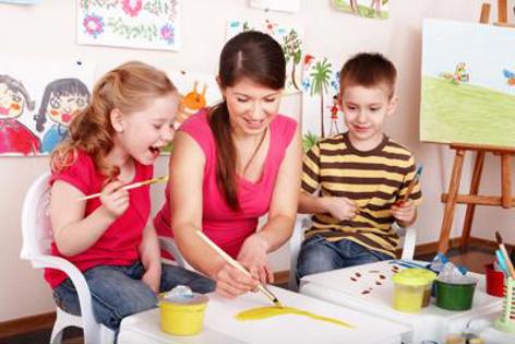 A nursery teacher and two children painting