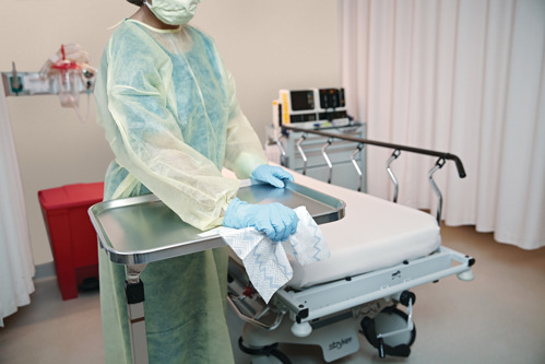 Cleaner in full PPE cleaning tray in hospital emergency room