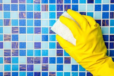 A hand in yellow rubber gloves scrubbing tiles