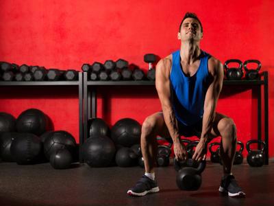 A man lifting a kettlebell in a room filled with gym equipment